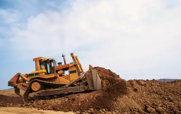 A yellow bulldozer pushes a large pile of dirt on a construction site under a partly cloudy sky. AdvanceTrac