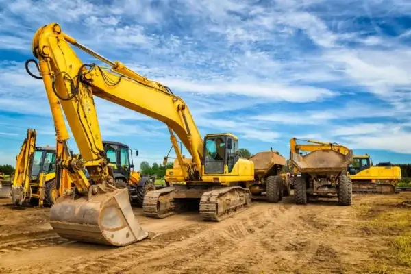 Several large yellow excavators and dump trucks are parked on a dirt construction site under a partly cloudy blue sky. AdvanceTrac