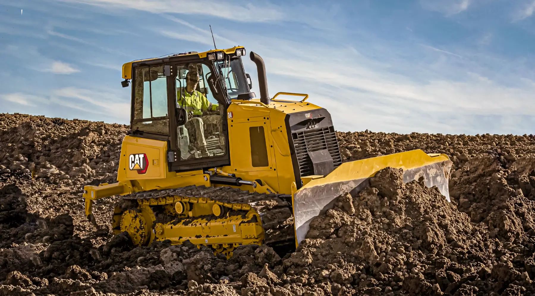 A yellow Caterpillar bulldozer pushes dirt at a construction site under a blue sky, operated by a person in a cab with glass windows. AdvanceTrac