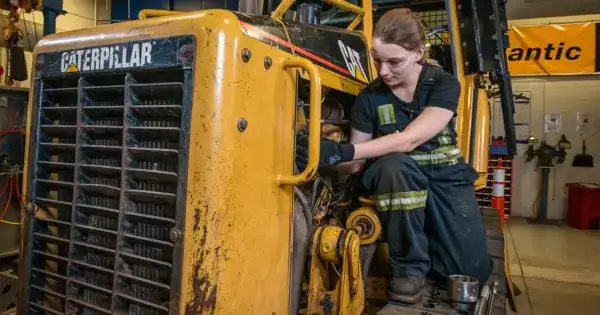 A person wearing safety glasses and gloves is repairing or inspecting the engine of a yellow Caterpillar construction vehicle in a workshop. AdvanceTrac