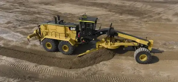 A yellow Caterpillar motor grader, one of the industry’s leading Motor Graders, levels dirt on a construction site, with large tires and a visible number 650 on top of the cab. AdvanceTrac