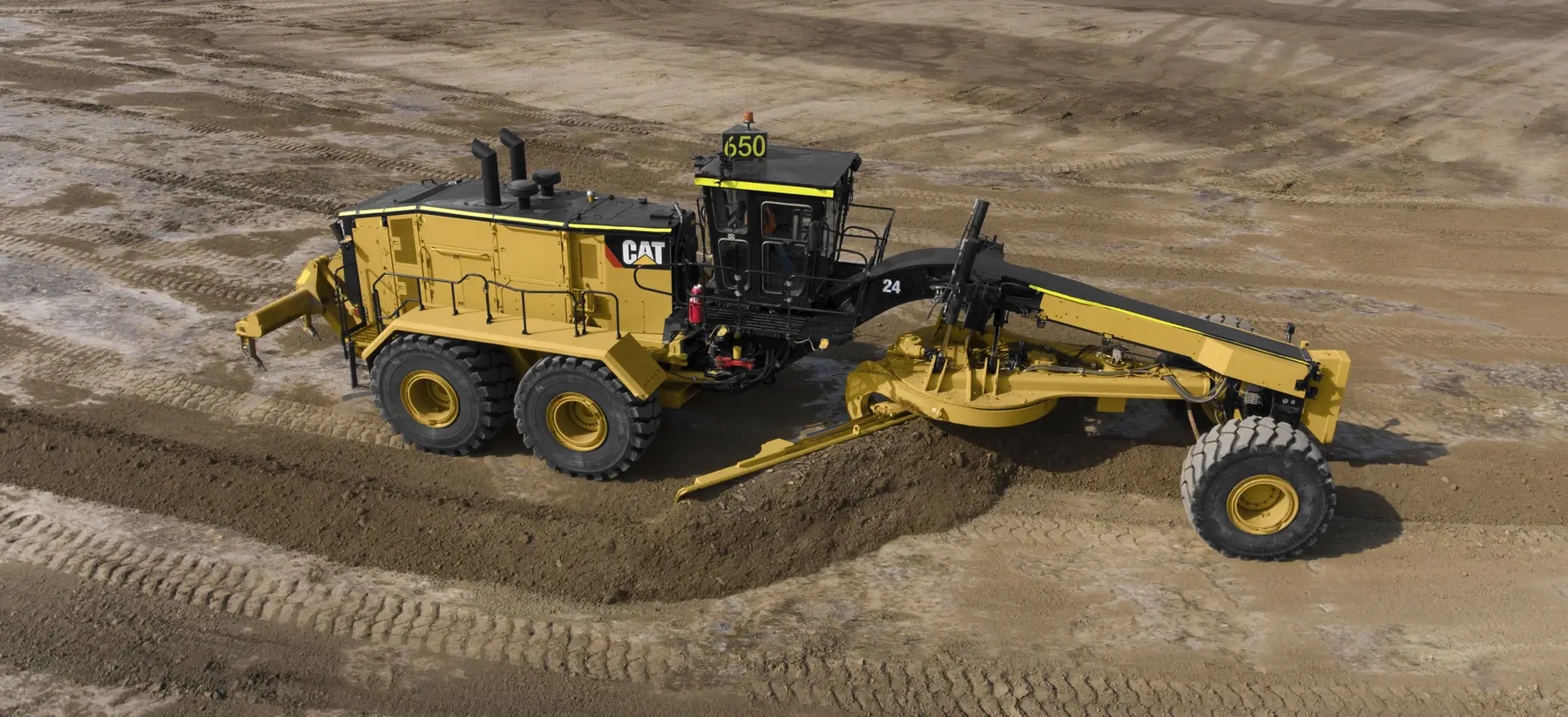 A yellow Caterpillar motor grader, one of the industry’s leading Motor Graders, levels dirt on a construction site, with large tires and a visible number 650 on top of the cab. AdvanceTrac