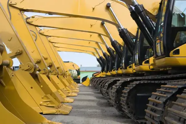 A row of yellow excavators is lined up outdoors on gravel, with their arms raised and tracks visible, creating a repeating geometric pattern. AdvanceTrac