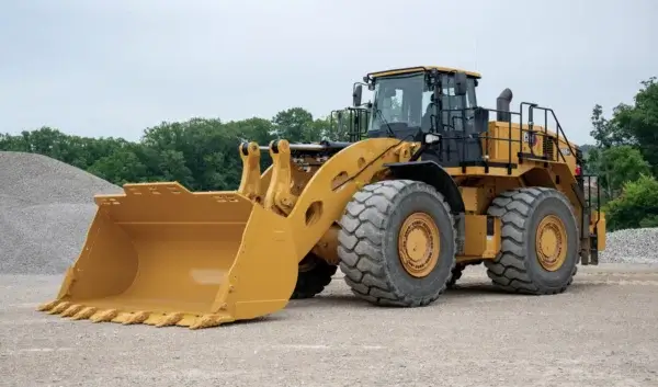 A large yellow front-end loader, one of the most robust wheel loaders, is parked on gravel, with big tires ready for any task and piles of stones and trees in the background. AdvanceTrac